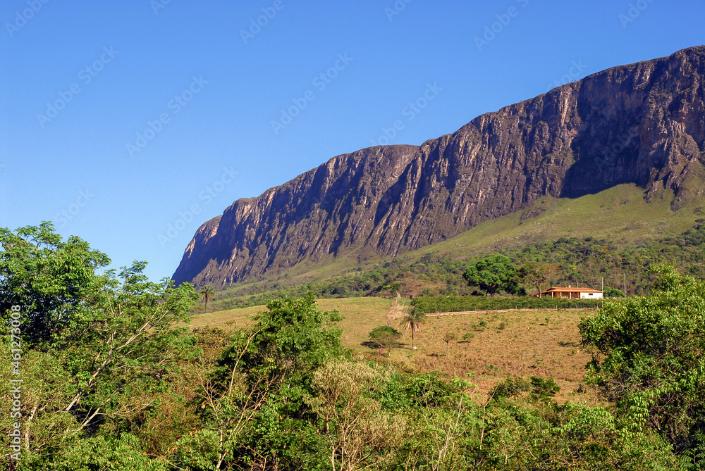 Large rock wall, from the Serra da Canastra park massif, with forest and pastures, sunny day and blue sky, São Roque de Minas, Minas Gerais, Brazil
