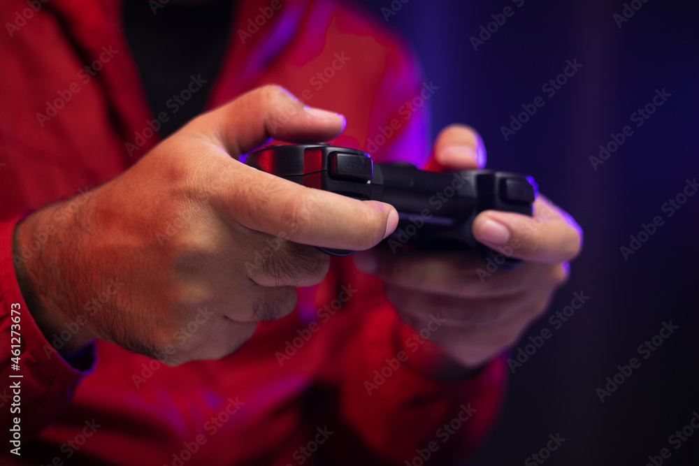 Close up male hands holding joystick game console. Young man playing video game online. Indian man in red jacket play computer pc at home in the dark room Close up male hands holding joystick game console. Young man playing video game online. Indian man in red jacket play computer pc at home in the dark room