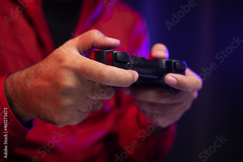 Close up male hands holding joystick game console. Young man playing video game online. Indian man in red jacket play computer pc at home in the dark room