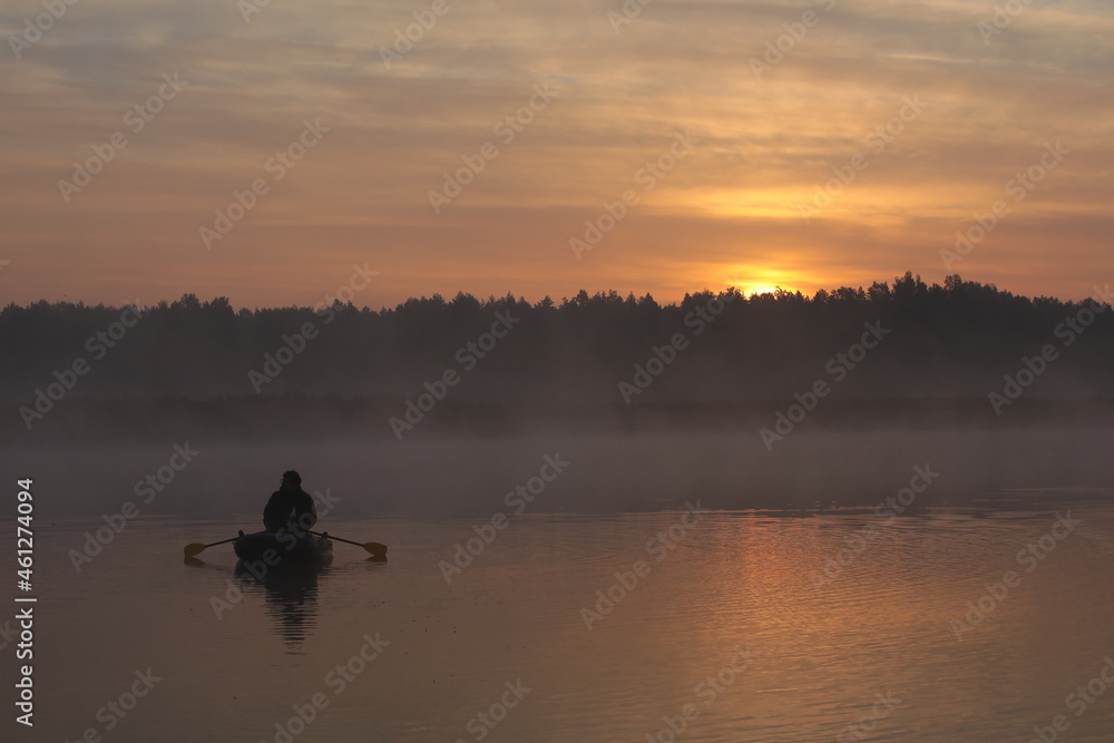 Fishing in the morning on the lake in the fog.Person floats in a boat at dawn in a pink haze