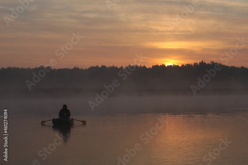 Fishing in the morning on the lake in the fog.Person floats in a boat at dawn in a pink haze © Nina