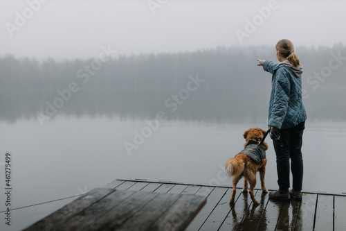 Pretty caucasian girl with brown Nova Scotia Duck Tolling Retriever staying on wooden pier and showing something to the dog with her hand. Leisure with dog. Selective focus, copy space. Pets concept.