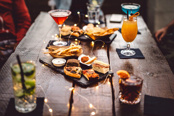 Blurred background of multicolored drinks and minimal food - Happy hour concept with fancy cocktails and tasty appetizers served at rooftop lounge prive - Warm vintage filter on shallow depth of field