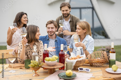 Pleased european friends talking and celebrating during friendly picnic. Young men and women drinking wine from glasses. Concept of friendship. Idea of leisure. Table with organic fruits