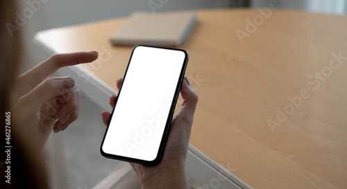 Mockup image blank white screen cell phone.women hand holding texting using mobile on desk at home office.