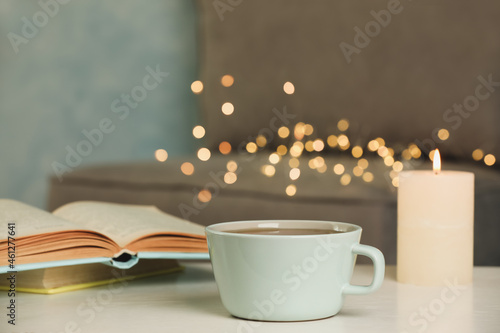 Cup of tasty freshly brewed tea, burning candle and open book on table