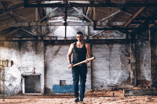 Strong Muscular Brutal Man in Black Tank Top with Baseball Bat Walks in Empty Grunge Hall