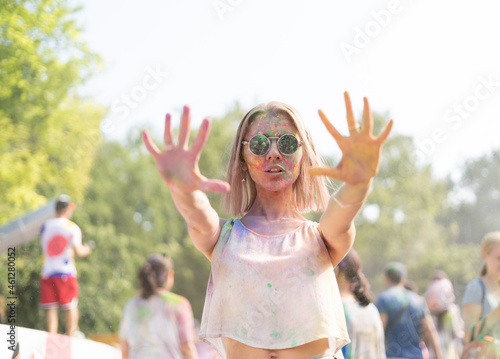 Millennial girl at the Holi Fest festival of paints in city park shows stop rocky. Traditional festival of dry urban paints. woman in glasses with face stained with paints photo