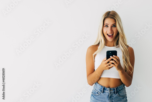 Surprised and excited woman gasping fascinated while reading message on mobile phone on white background
