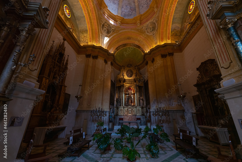 Obraz premium A side wing in the interior of the old historic church of Felanitx on the Spanish Mediterranean island of Mallorca. At the back is an altar with gold decorations.