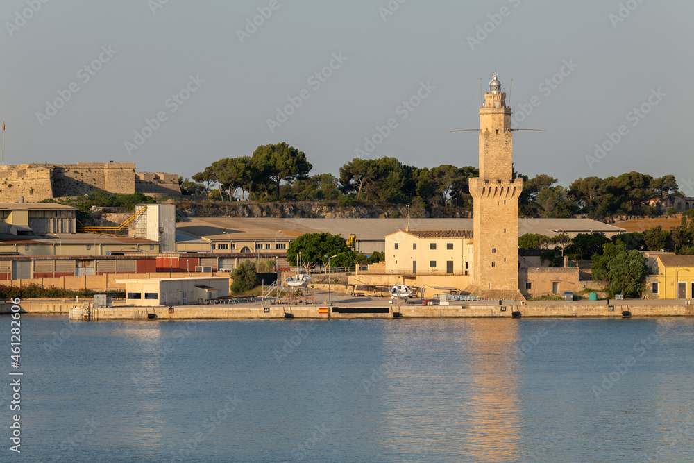 In the morning after sunrise in the port of Palma on the Mediterranean island of Mallorca. A lighthouse made of stones stands behind the quay wall. Sailboats are on land.