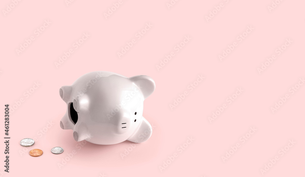 fallen piggy bank with US coins coming out, white piggy with pink background bottom left corner fallen piggy bank with US coins coming out, white piggy with pink background bottom left corner