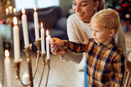 Happy mother assists her small son to light up candles in menorah during Hanukkah celebration. photo