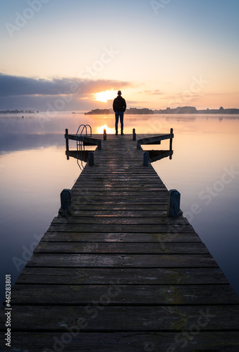 A man looking over a lake during a foggy, tranquil morning.