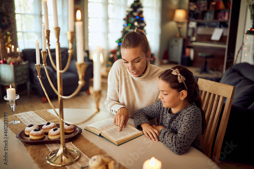 Jewish mother and daughter read Tanakh during Hanukkah at home. photo