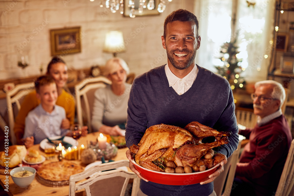 Happy man holds Thanksgiving turkey while having family meal in dining room. Happy man holds Thanksgiving turkey while having family meal in dining room.