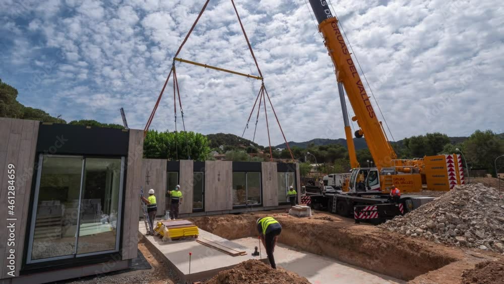 Timelapse construction workers directing contemporary housing module suspended by crane lift onto development site