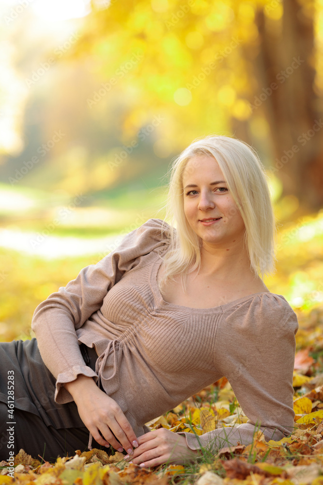 blonde girl in street clothes sitting in a heap of autumn leaves blonde girl in street clothes sitting in a heap of autumn leaves