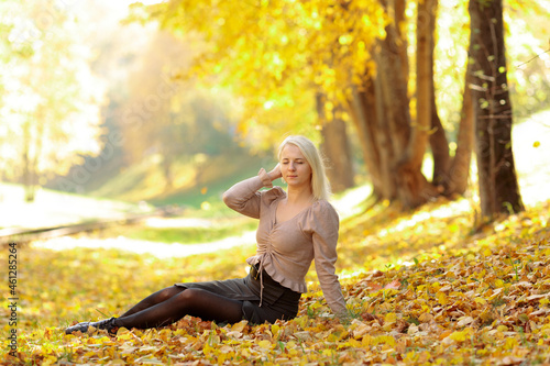 blonde girl in street clothes sitting in a heap of autumn leaves