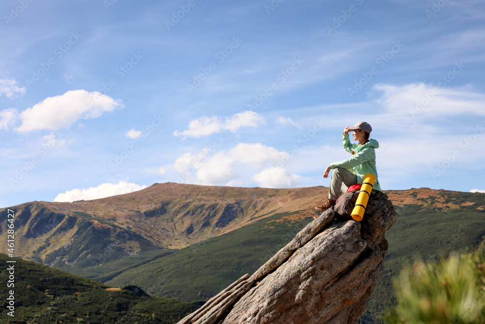 Young woman with backpack on rocky peak in mountains. Space for text Young woman with backpack on rocky peak in mountains. Space for text