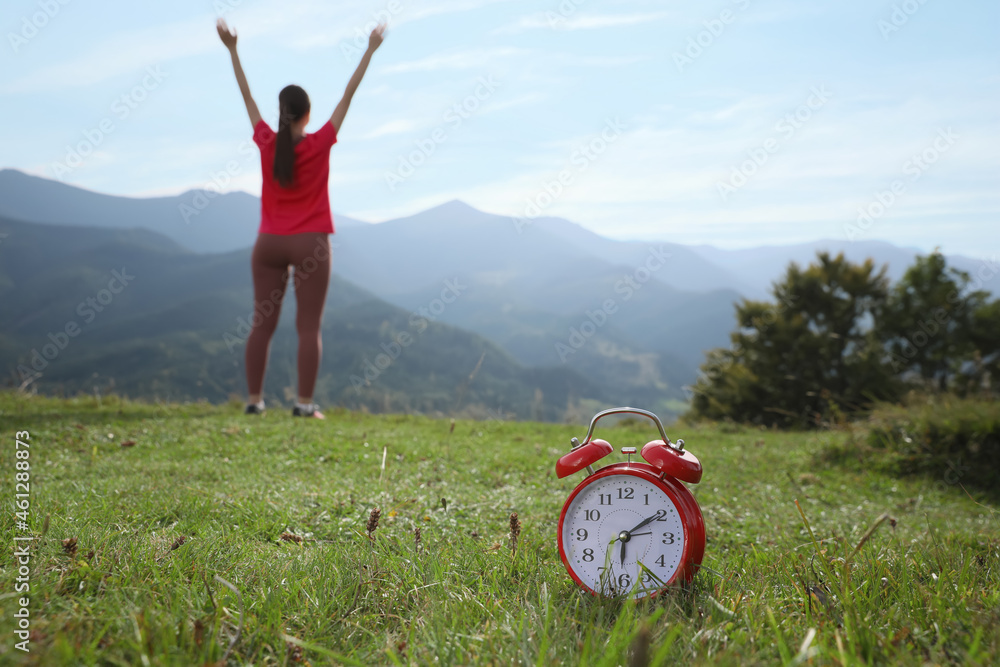 Woman doing morning exercise in mountains, focus on alarm clock - obrazy, fototapety, plakaty 