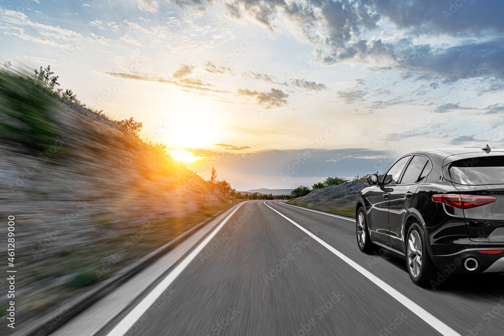 Gray car on a scenic road. Car on the road surrounded by a magnificent natural landscape in the rays of sunset or dawn.