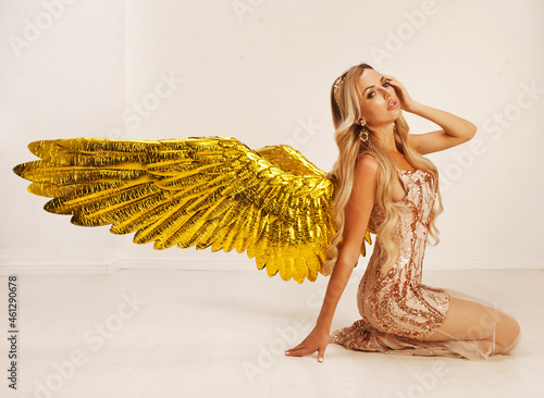 A beautiful young model with big golden angel wings is sitting in the studio. white background photo