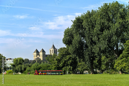 Colorful park train surrounded by greenery and St. Kunibert church in the far distance in Cologne photo