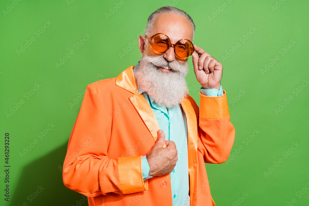 Portrait of attractive cheerful grey-haired man touching orange specs posing isolated over bright green color background - obrazy, fototapety, plakaty 