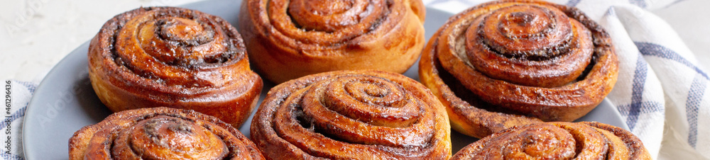 Fototapeta premium banner of baked cinnamon buns on grey plate on light background with checkered napkin