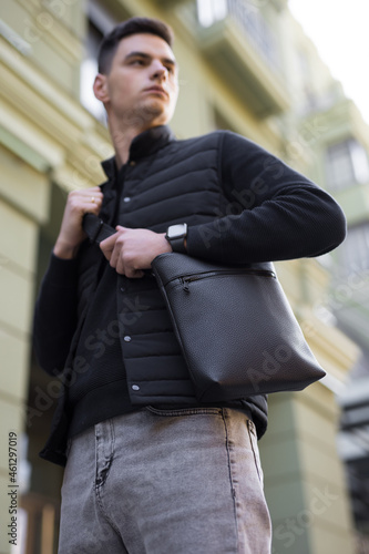 Man holding black leather messenger bag in a city