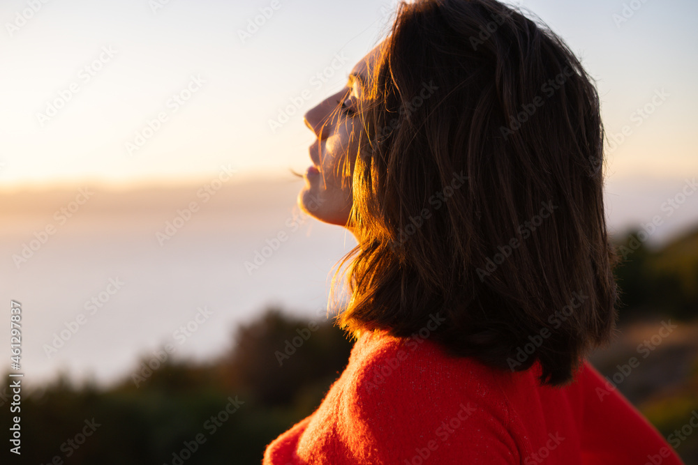 Young woman in a red sweater at a magnificent sunset on the mountain against the background of the sea, romantic mood, smiling happily
