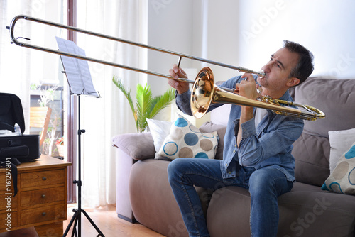 Novice man playing trombone at home with enthusiasm