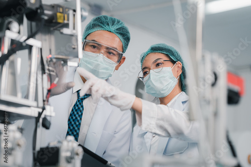 Both male and female Asian scientists are outfitted with protective gear. Examining the factory's machinery and materials used in the mask-making process. Covid 19 is a piece of preventive equipment.