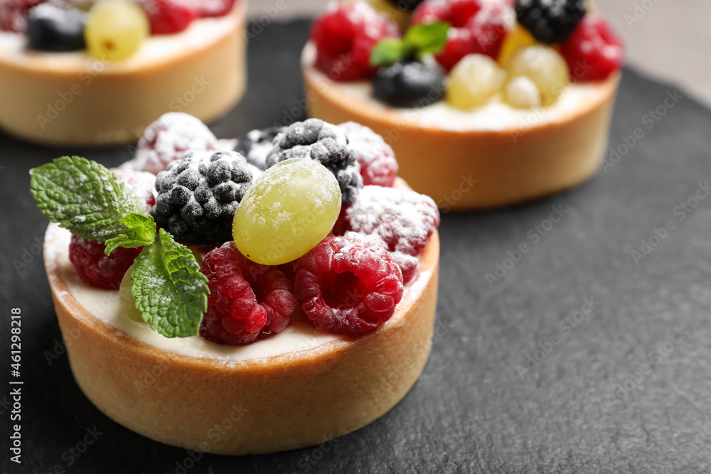 Delicious tartlets with berries on slate board, closeup Delicious tartlets with berries on slate board, closeup