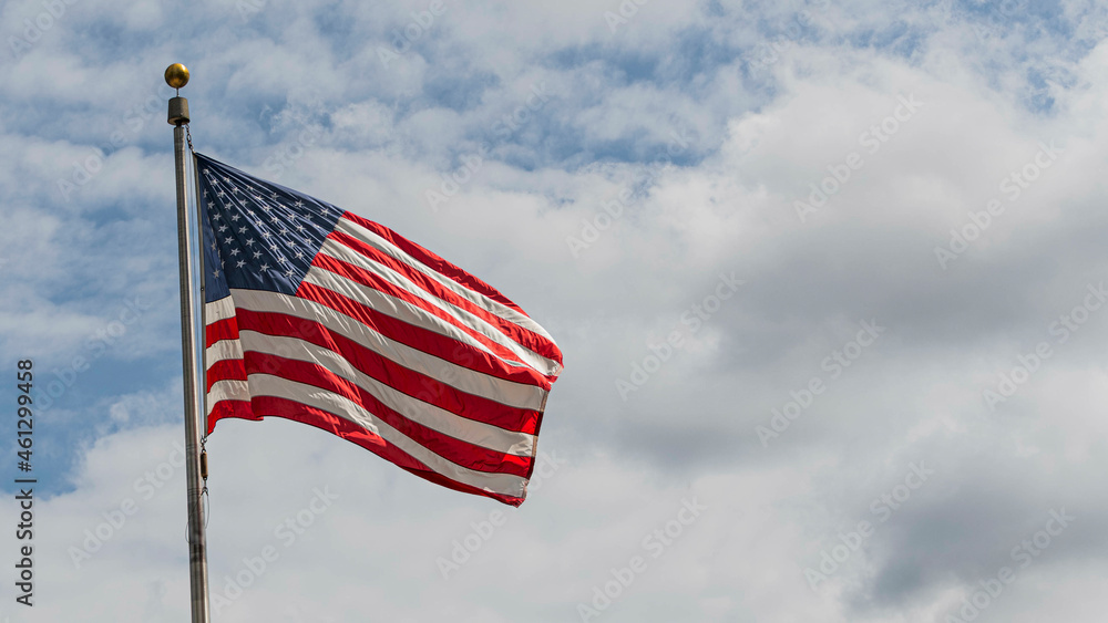 Flag of the United States of America flying in the wind on a cloudy sky  background.