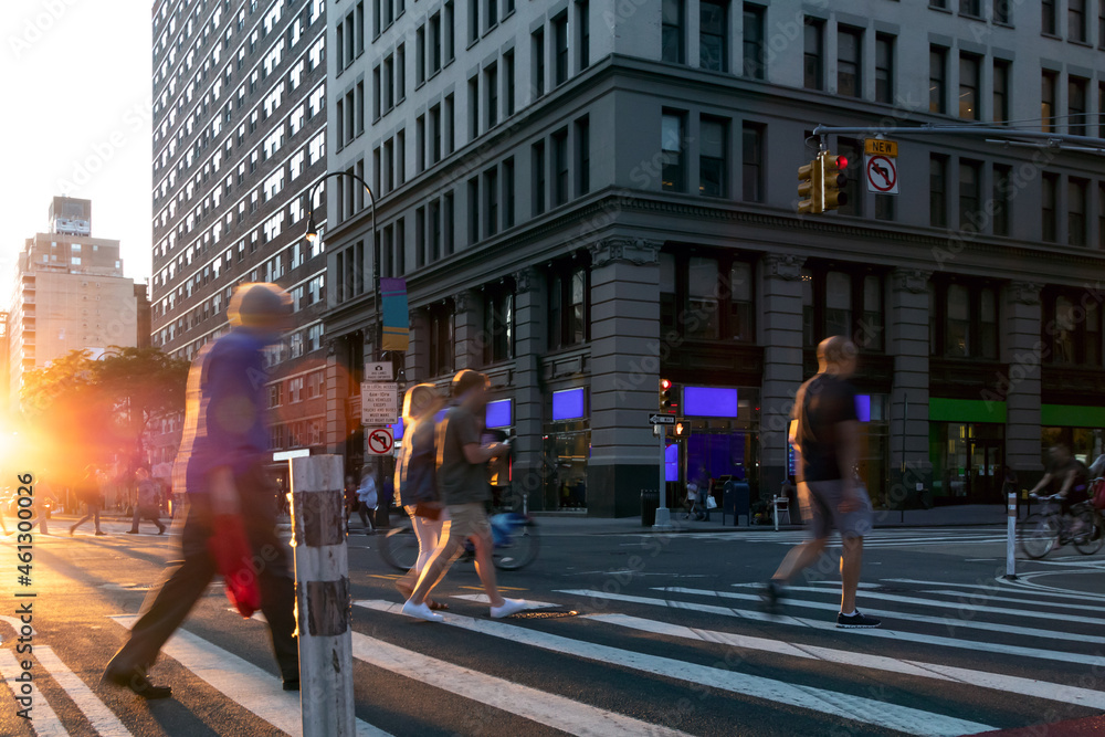 Busy intersection with people walking through the crosswalk on 14th Street and 5th Avenue in New York City with sunlight background