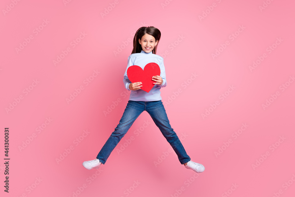 Full length body size view of attractive cheerful trendy girl jumping holding heart isolated over pink color background
