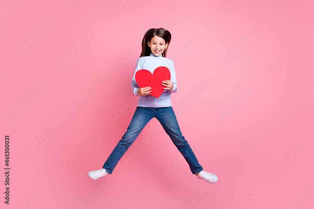 Full length body size view of attractive cheerful trendy girl jumping holding heart isolated over pink color background Full length body size view of attractive cheerful trendy girl jumping holding heart isolated over pink color background