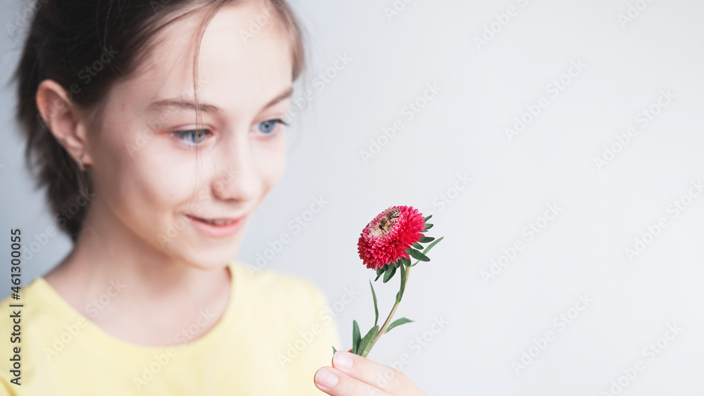 A bee sits on an aster, a teenage girl holds a flower with curiosity in her hands selective focus
