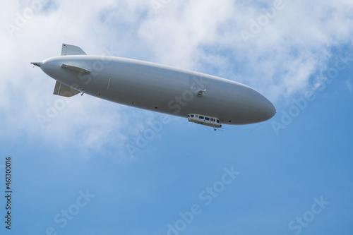Gray cigar-shaped airship flying in blue sky under clouds photo