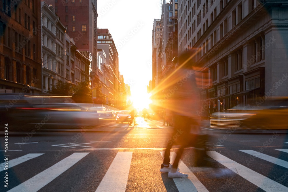 People and cars crossing the busy intersection on 5th Avenue with sunset light shining on 5th Avenue in Manhattan, New York City