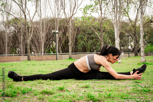 Beautiful young Latin woman doing muscle stretching exercises and position in a fitness session on the grass of a public square. Concept of healthy life, healthy lifestyle,