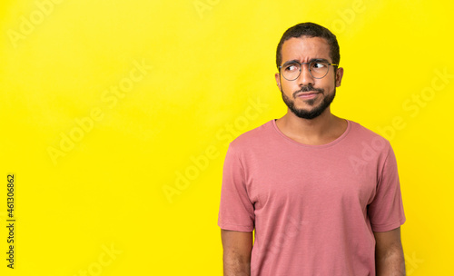 Young latin man isolated on yellow background having doubts while looking side