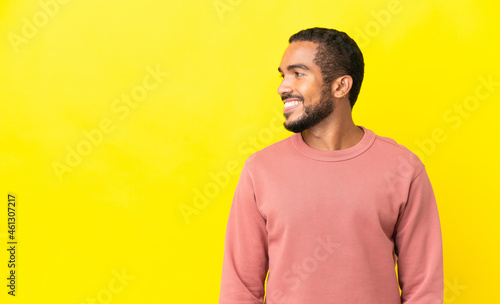 Young latin man isolated on yellow background looking side