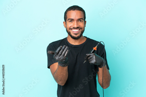 Tattoo artist Ecuadorian man isolated on blue background inviting to come with hand. Happy that you came