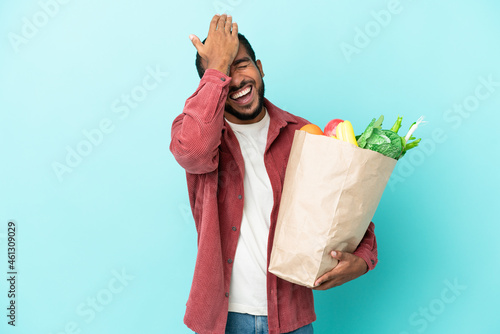 Young latin man holding a grocery shopping bag isolated on blue background has realized something and intending the solution