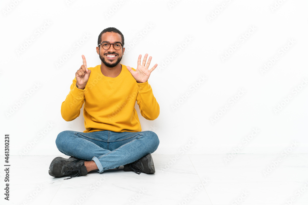 Young Ecuadorian man sitting on the floor isolated on white wall counting six with fingers Young Ecuadorian man sitting on the floor isolated on white wall counting six with fingers