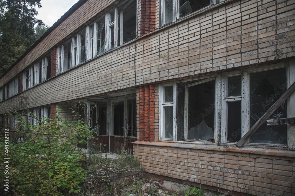 Abandoned brick building in the forest. Blue sky. Sunny day. Facade of an abandoned building. Green trees and grass.