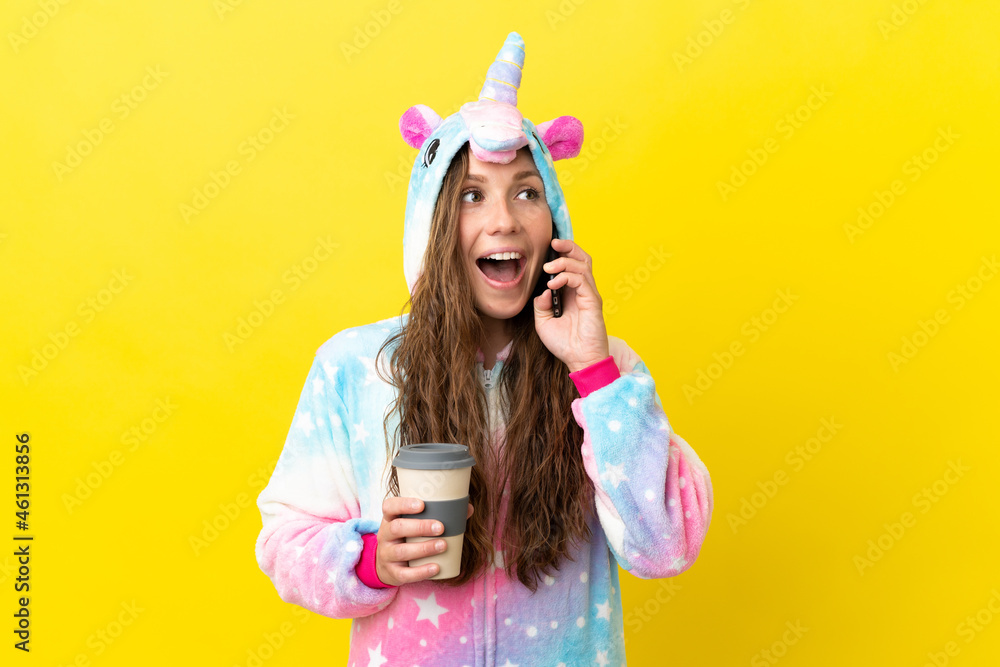 Girl with unicorn pajamas over isolated background holding coffee to take away and a mobile Girl with unicorn pajamas over isolated background holding coffee to take away and a mobile